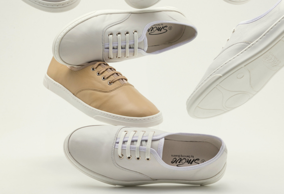 Schwebende weiß-beige Sneaker mit Schnürsenkeln vor neutralem Hintergrund.